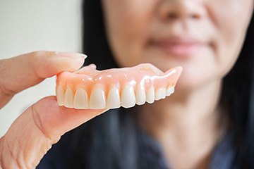 Close up of woman holding denture in Naples, FL