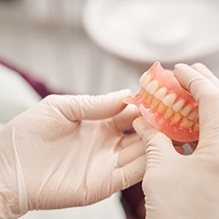 Gloved hands holding dentures in Naples, FL