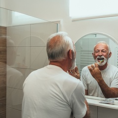 Man smiling while brushing his teeth in bathroom